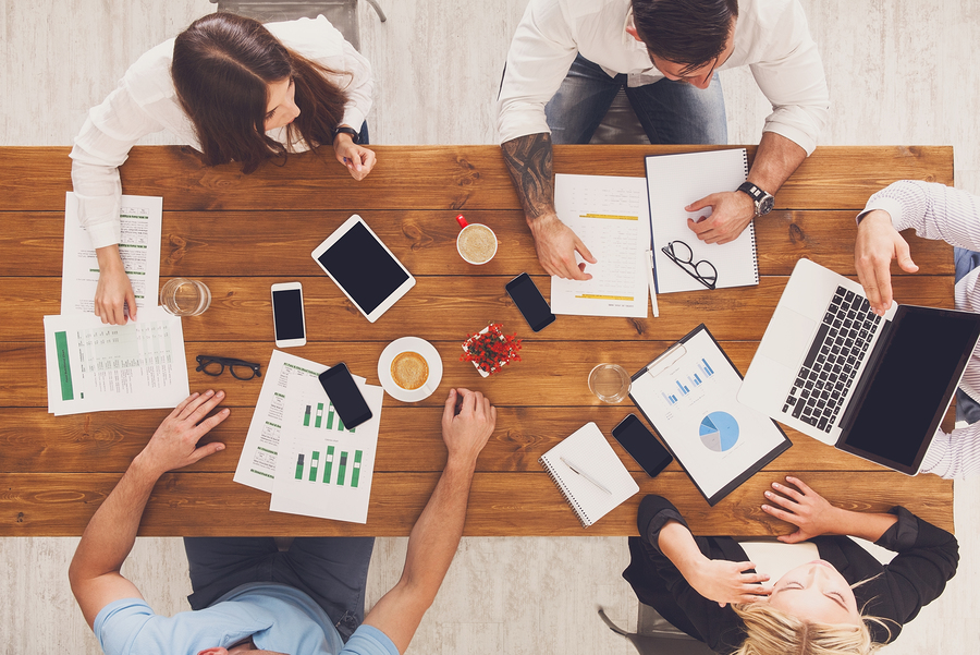 Group of busy business people working in office, top view of wooden table with mobile phones, laptop, tablet and documents papers with diagram. Men and women team together have brainstorm discussion.