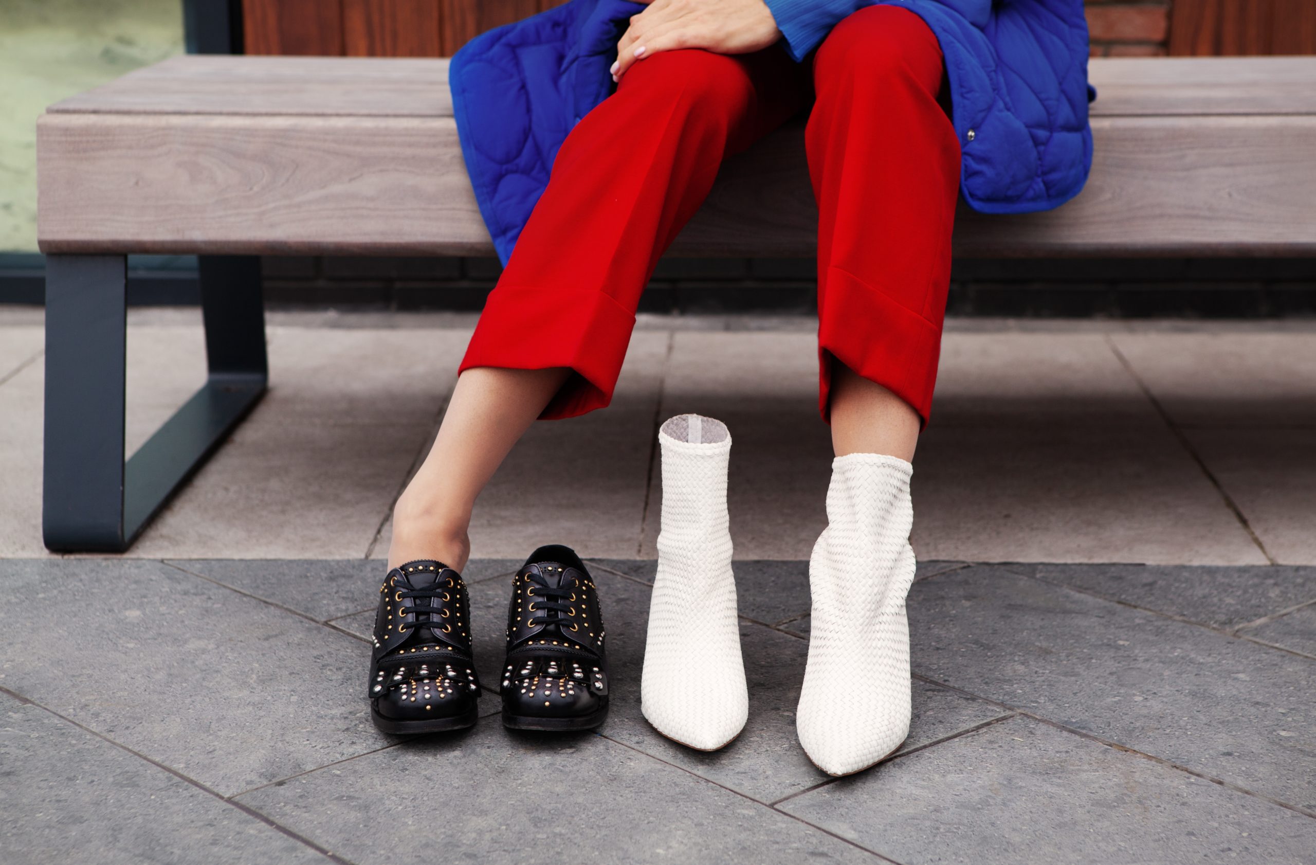 Woman chooses shoes. Close up female legs, trendy leather white and black boots with rivets